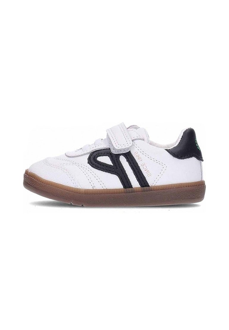 Zapatillas blancas para niños con rayas laterales negras, suela marrón y cierre de tira de velcro.