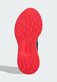 Semelle de chaussure noire avec un motif de relief, dotée d'une semelle extérieure rouge vif et d'une silhouette épurée. Matériaux durables, conception légère.
