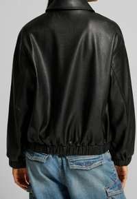 Svart läder bomberjacka med krage, elastisk midja och lösa ärmar, parat med ljusblå cargobyxor.