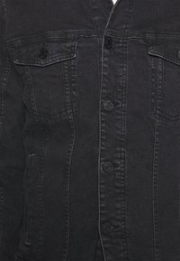 Giacca in denim nera caratterizzata da una chiusura con bottoni frontali, due tasche sul petto e dettagli di cuciture sottili. Tessuto texturizzato con una silhouette aderente.