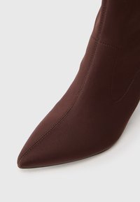 Spidse tå ankelstøvle i mørkebrunt stof, med en glat tekstur og diskret syningsdetalje, designet til en tætsiddende silhuet.