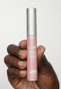 Olej do ust w cylindrycznej różowej tubie z metalową srebrną zakrętką; tekst wyświetla "OLEJ DO UST" oraz "huile pour le levres". Produkt jest trzymany w ręce w sposób wyraźny.