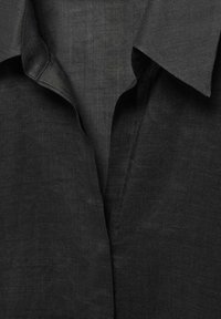 Primer plano del cuello de una camisa de lino negra, que presenta un acabado texturizado, diseño clásico, con un cuello bien doblado y una caída suave.