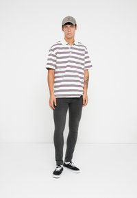 Camisa polo a rayas con líneas blancas, moradas y marinas, de mangas cortas y cuello; combinada con jeans oscuros de corte ajustado y zapatillas negras.