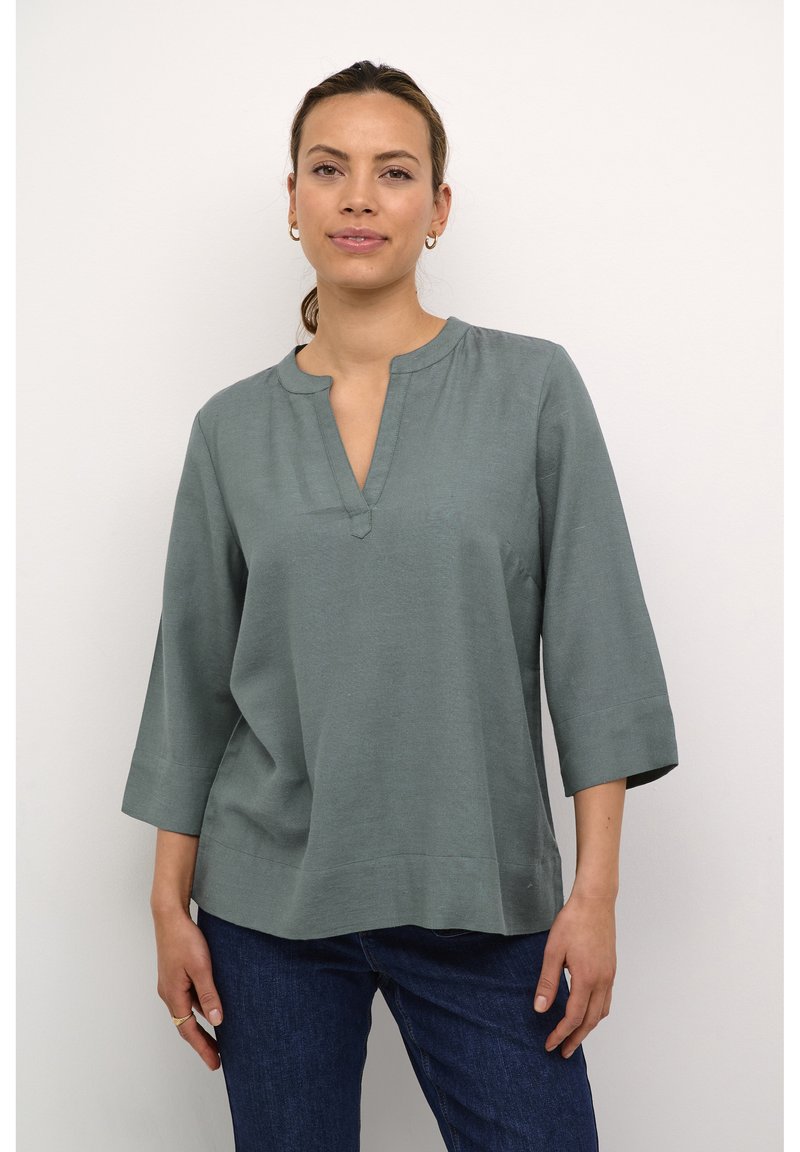 Blusa di colore verde chiaro, morbida e con una vestibilità ampia, scollo tondo e maniche a tre quarti. Texture liscia, dettagli minimi e forma rilassata.