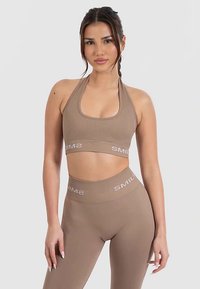 Beiger athletischer Crop-Top und Leggings mit gerippter Textur und Logo. Das Top hat ein Neckholder-Design, während die Leggings hoch tailliert sind.