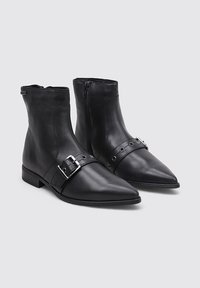 Bottines en cuir noir avec des orteils pointus, des fermetures à glissière sur les côtés, des talons bas et des sangles décoratives en boucle sur le devant.