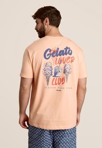 Perzikkleurig katoen t-shirt met een achterkantprint van kleurrijke gelato-ijshoorntjes en de tekst "Gelato Lover Club" in blauw en rood. Korte mouwen en ronde hals.