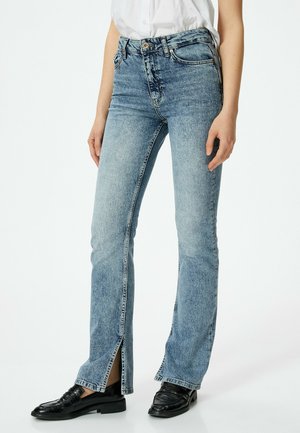 Jeans de mezclilla azul claro de corte acampanado con aberturas frontales en el dobladillo, cinco bolsillos, herrajes plateados y un diseño de cintura alta. Acabado texturizado.
