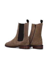 Bottes chelsea en suede brun avec panneaux élastiques sur les côtés, détails en brogue et fermeture éclair à l'arrière, arborant un talon en bois et une finition texturée.