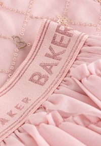 Rosa Kleidungsstück mit einer strukturierten Stoffoberfläche und einem Diamantmuster, verziert mit kleinen goldenen Pailletten. Rüschensaum und ein Etikett mit der Aufschrift "BAKER".