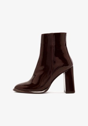 Bottine en cuir verni bourgogne avec un bout rond et un talon bloc transparent. Présente des coutures rouges visibles le long de la couture latérale.