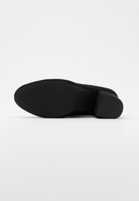 Zapato de tacón alto negro con un upper suave y texturizado, una punta afilada y una suela de goma. El tacón es corto y de forma cuadrada.