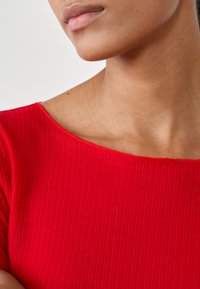 Czerwona bluzka ze strukturalnym ribbingiem, z szerokim dekoltem i teksturowanym materiałem, podkreślająca miękkie żłobienia i bezszwowy design.