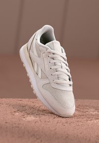 Baskets blanches avec une tige en daim perforé, bout arrondi, lacets plats et semelle rembourrée. Caractérisées par un logo discret sur le côté.