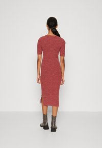 Rotes geripptes Strickkleid mit kurzen Ärmeln, figurbetontem Design, seitlichem Schlitz und getragen mit grauen Stiefeletten.