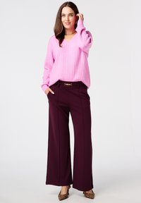 Roze geribbelde gebreide trui met een V-hals, gecombineerd met burgundy wijde broek met een gouden accent op de riem en laarsjes met luipaardprint.