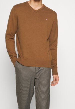Brun v-hals sweater i blødt materiale med ribbet manchetter og kant, kombineret med ternede bukser i sort og hvidt mønster.