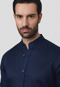 Granatowa koszula zapinana na guziki z kołnierzykiem mandarynkowym; gładka tekstura materiału; z małymi okrągłymi guzikami wzdłuż przodu.