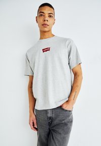 Grå bomulds t-shirt med korte ærmer, med et rødt Levi's logo mærke på brystet. Kombination med mørkegrå jeans.