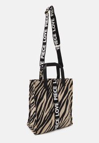 Sac cabas à rayures zébrées tan et noir avec poignées noires et une bandoulière portant le texte "LOVE PIECE" en blanc. Fabriqué en tissu résistant.