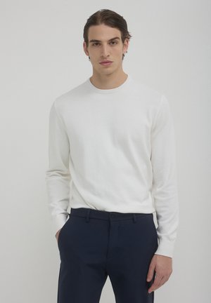 Chemise blanche à manches longues avec un col rond, texture lisse, associée à un pantalon bleu marine foncé. Design simple et ajusté sans motifs.