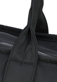 Czarna torba z tkaniny z grubymi, teksturowanymi paskami, posiadająca wzmocnione szwy i gładkie wnętrze. Projekt jest prosty i funkcjonalny.