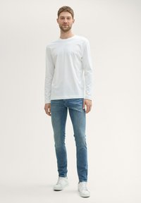 Camisa blanca de manga larga, diseño ajustado; combinada con jeans skinny de color azul claro y zapatillas blancas. Textura lisa, estilo minimalista.