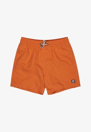 Blond chłopiec stojący boso, ubrany w biały krótki rashguard z logo oraz pomarańczowe spodenki kąpielowe z sznurkiem.