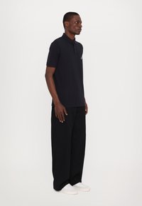 Marineblå polo med korte ermer og krage, kombinert med svarte vide bukser og hvite joggesko. Minimalistisk design, ingen synlige mønstre.