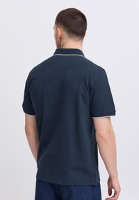 Mörk marinblå polo med korta ärmar, texturerat tyg och ljusgrå kant på kragen och ärmarna. Standardpassform, avslappnad design.