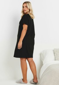Abito nero a maniche corte con una vestibilità morbida, tessuto liscio e lunghezza al ginocchio. Indossato con pantofole grigie pelose. Design semplice.