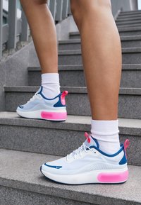 Nohy obuté do bílých a modrých tenisek s růžovými akcenty stoupající po šedých venkovních schodech.
