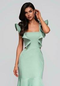 Robe mint verte élégante avec des manches à volants, un décolleté carré et une silhouette ajustée, comportant un ourlet évasé et une texture douce.