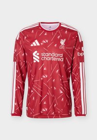 Κόκκινη φανέλα ποδοσφαίρου Liverpool FC με μακριά μανίκια, λευκά γεωμετρικά σχέδια, λογότυπο Adidas, χορηγό Standard Chartered και λευκές ρίγες στα μανίκια.