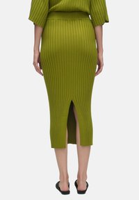 Jupe midi tricotée côtelée verte avec une fente à l'arrière, dotée d'une silhouette ajustée et d'un design taille haute. Texture douce avec des lignes verticales.