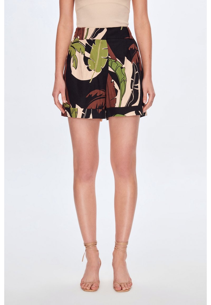 Femme portant un short taille haute imprimé de feuilles tropicales vertes, marron et beige, associé à des talons beiges à brides et un haut beige sans manches.