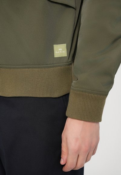 Õliveroheline bomber-jakk soonikkoes mansettide ja äärega. Varustatud väikese ruudukujulise sildiga, millel on helerohelisel taustal kiri "PS Paul Smith".