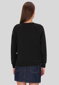 Fekete pulóver raglán ujjakkal, bordázott gallérral és mandzsettákkal, farmer miniszoknyával kombinálva, amely zsebekkel és rojtos szegéllyel rendelkezik.