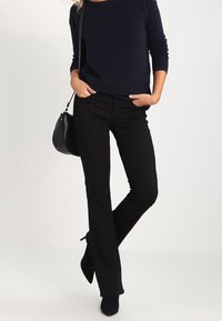 Pantaloni neri a palazzo abbinati a un top a maniche lunghe blu navy a coste. Una piccola borsa nera e scarpe nere completano l'outfit.