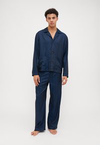 Navy blue silk pajama set with vertical stripes, featuring a buttoned shirt with a collar and two front pockets, complemented by loose-fitting pants.