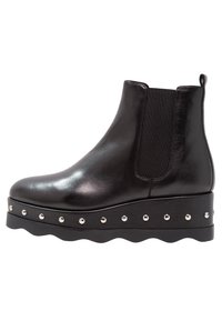 Botín Chelsea de cuero negro con paneles laterales elásticos, suela gruesa y remaches plateados a lo largo del borde. Diseño elegante y moderno.
