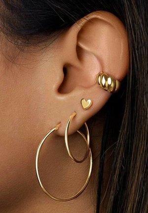 Goldene Creolen mit glatter Oberfläche und dünnem Design, begleitet von einem kleinen goldenen Herzstecker, auf der Haut präsentiert.