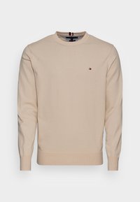 Maglione in cotone beige con maniche lunghe, scollo rotondo, polsini e orlo a costine, con un piccolo logo rosso, bianco e blu sul petto.