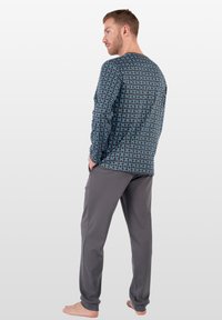 Blaues und schwarzes langärmeliges Shirt mit geometrischem Muster, kombiniert mit grauen Hosen. Der Stoff wirkt weich, hat eine lockere Passform und Taschen.