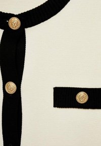 Knit cardigan featuring a cream body with black accents, a round neckline, and gold decorative buttons with embossed details.
