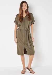 Olivgrünes Midikleid mit kurzen Ärmeln, knöpfbarem Vorderteil, geraffter Taille und einem Bindegürtel. Glattes Material mit einem leichten Glanz.