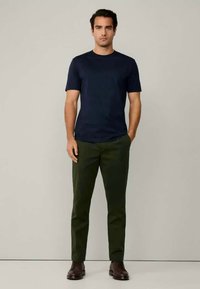 T-shirt de manga curta azul-marinho combinado com calças verde-oliva. O conjunto tem um corte clássico e é complementado por calçado castanho.