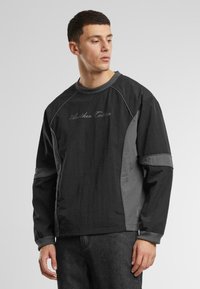 Pulover negru cu accente gri, mâneci lungi, design raglan și textul logo "Another Cotton" în gri pe față. Țesătură texturată.