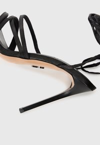 Čierne vysoké sandále na ihlovom podpätku s elegantným dizajnom, s hladkou podrážkou a špicatou špičkou. Obsahujú tenké remienky a stiletto podpätok.